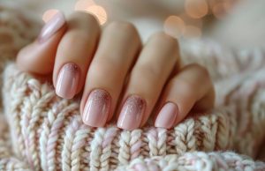 close up pink glitter nail polish womans hand resting knitted sweater